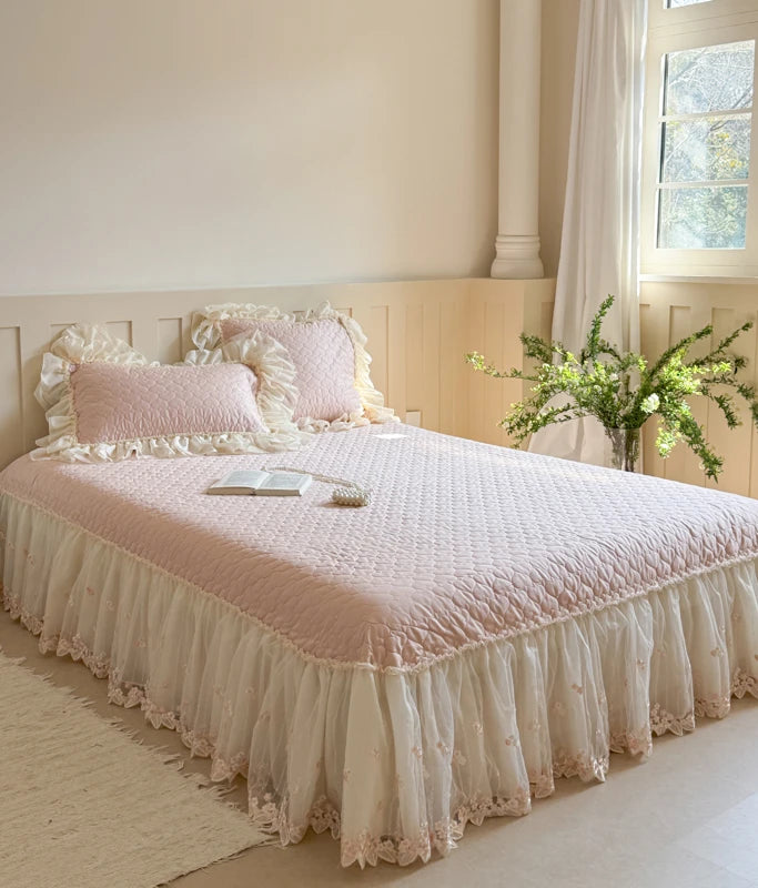 Bed with pink ruffled bedspread and white pillows in a bright room.