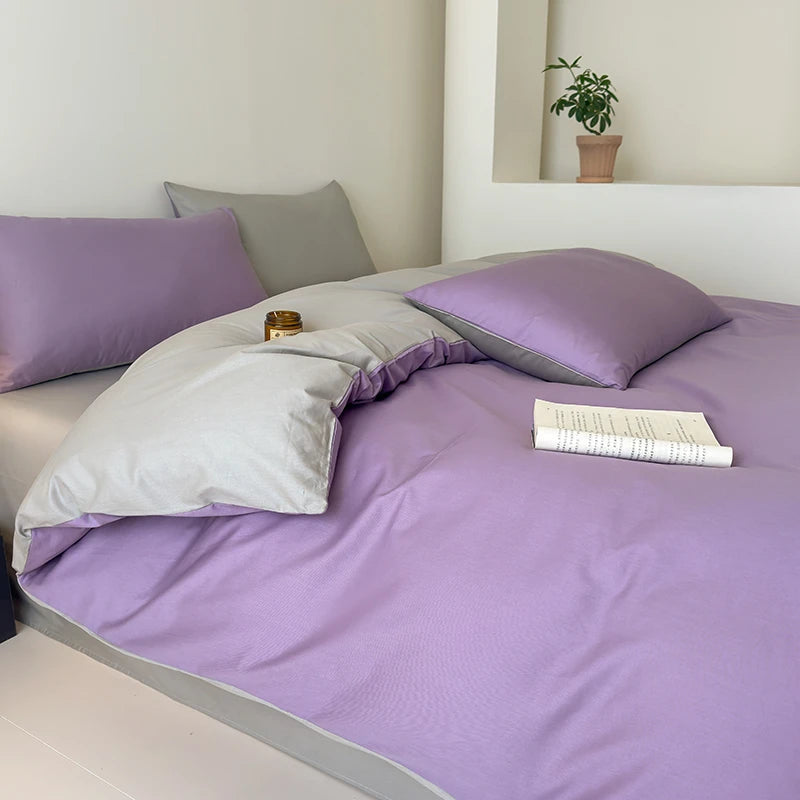 Bed with purple bedding and gray pillows in a minimalistic room.
