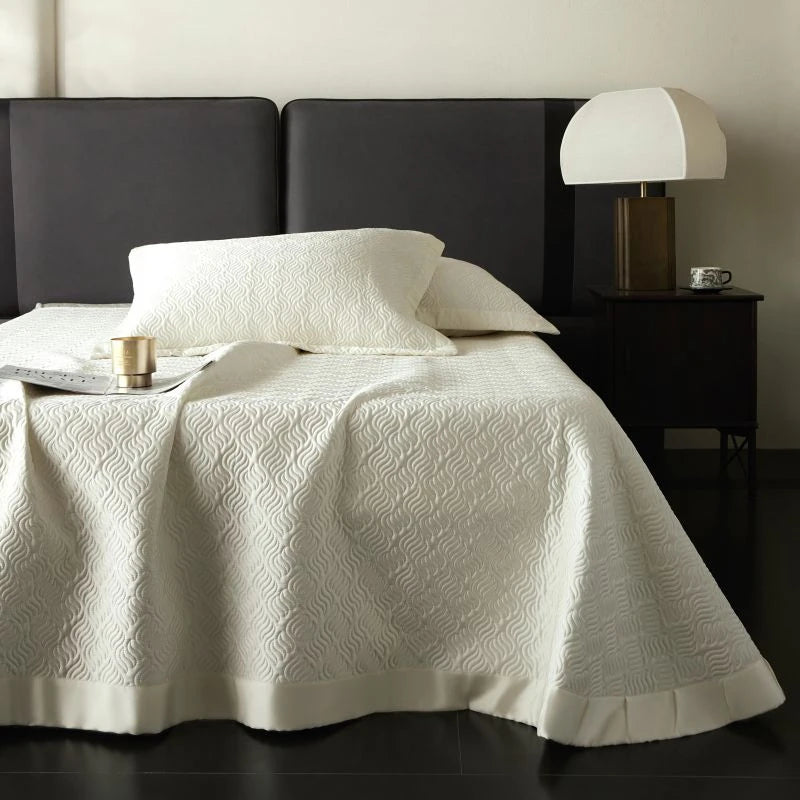 Bed with white textured bed spread and pillows.