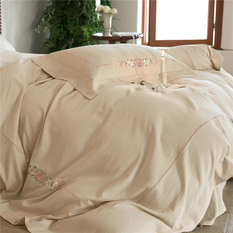 Beige bedding set with floral embroidery on a bed in a bedroom setting.