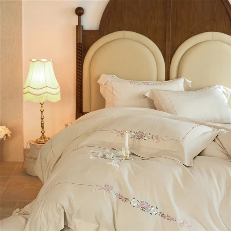 Beige embroidered bedding set on a bed with a wooden headboard and lamp in a bedroom.