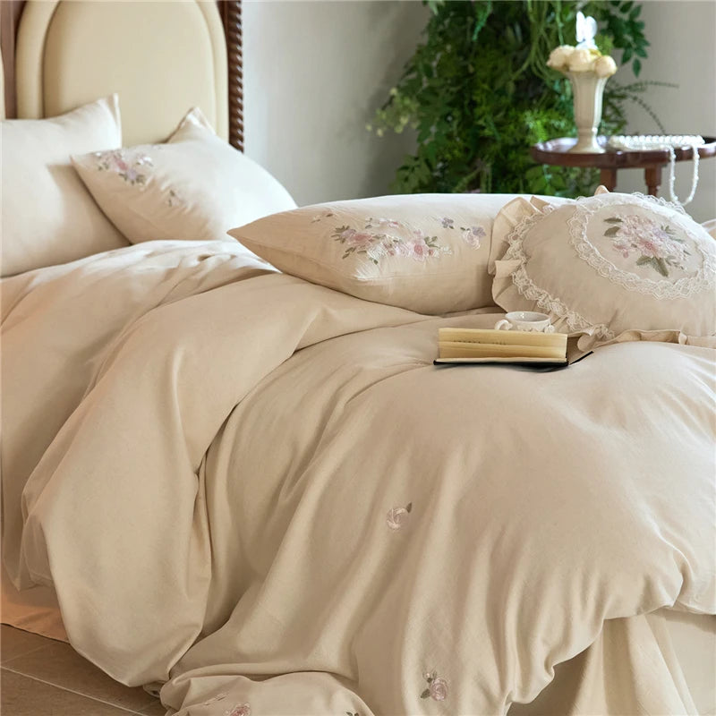 Beige floral embroidered bedding set on a bed with a blurred background
