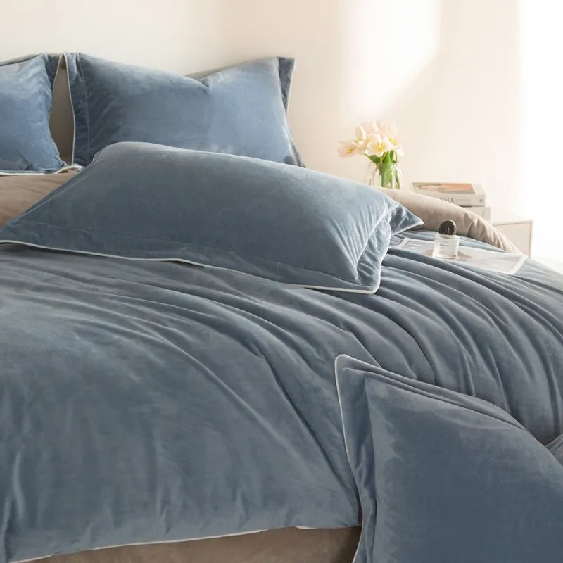 Blue velvet bedding set on a bed with pillows and a lamp in the background.