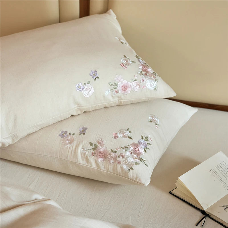 Floral embroidered pillow cases on a bed with an open book.
