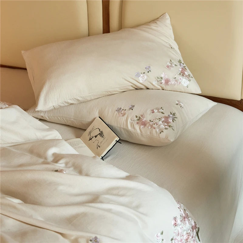 Floral embroidered pillows and bedding on a bed with a beige headboard.