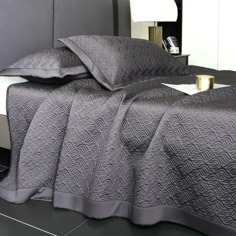Gray quilt bed spread with geometric pattern on a bed in a bedroom setting.