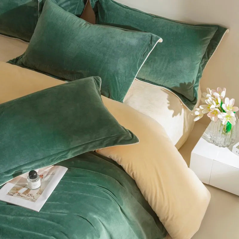 Green velvet pillows on a bed with a small plant and book in the background.