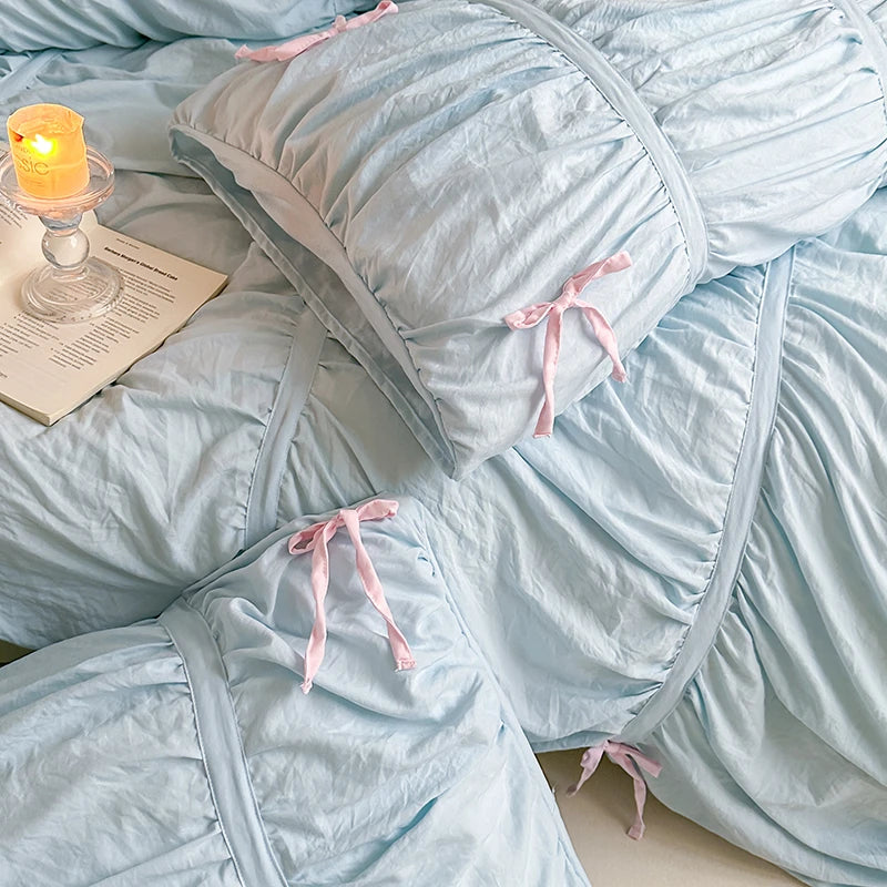 Light blue bedding set with pink ties on a bed, accompanied by a lit candle and a book.