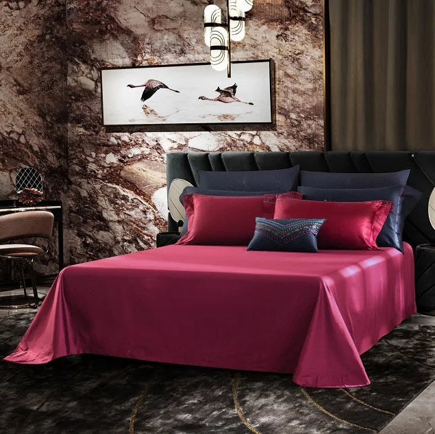 Modern bedroom with red wine bedspread and colorful pillows against a textured wall.