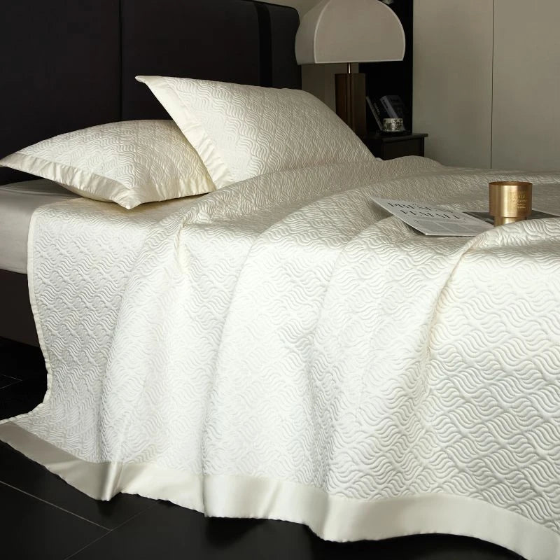 Neatly made bed with white textured bedding and pillows in a bedroom setting.