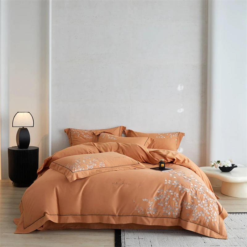 Orange floral bedspread on a bed in a bedroom with a lamp and side table.