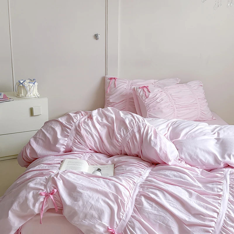 Pink bedspread with bow details on a bed in a room.