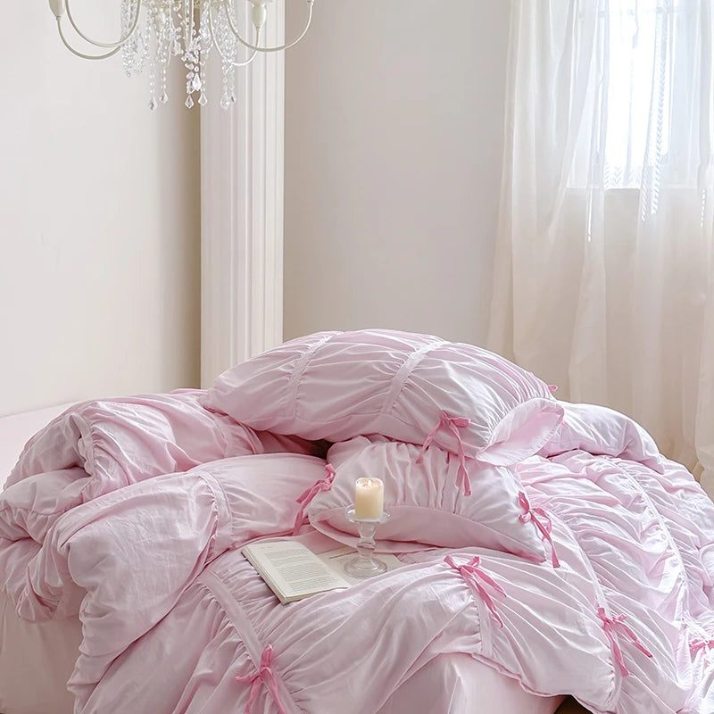 Pink bedspread with bow details on a bed in a softly lit room.