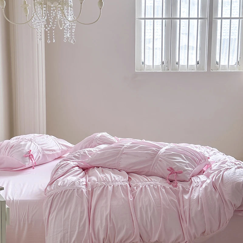 Pink comforter on a bed in a bright room with a chandelier.