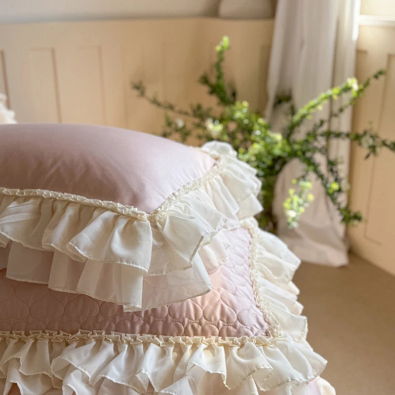 Pink ruffled Egyptian cotton pillowcases with lace trim on a bed in a softly lit room.