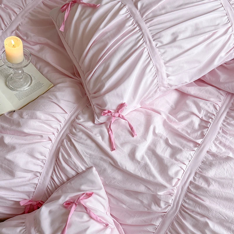 Pink ruffled bedding set with a candle and book on a bed