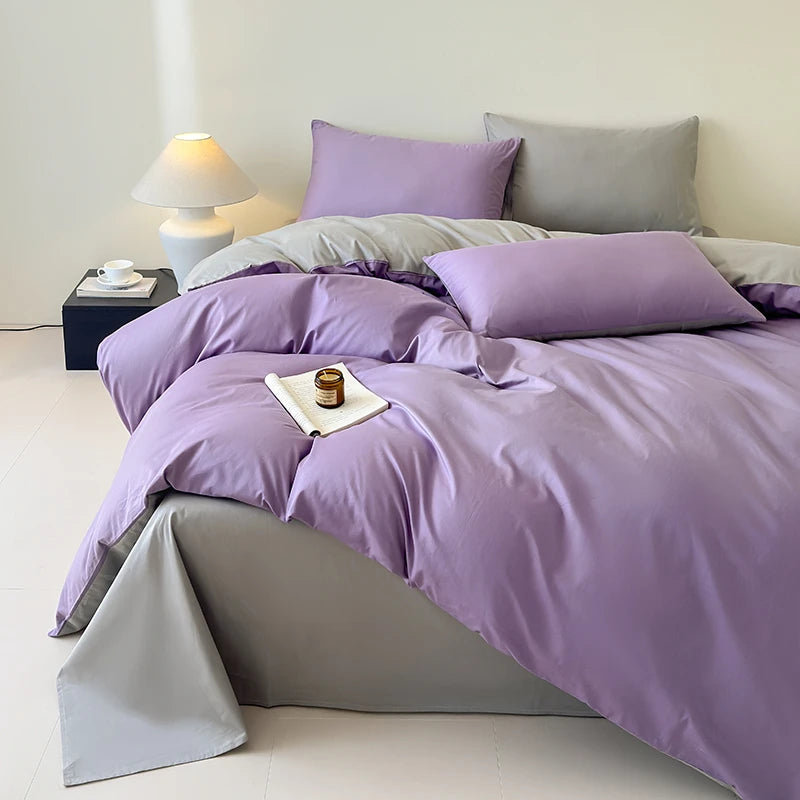 Purple bedding set on a bed with a nightstand and lamp in the background.