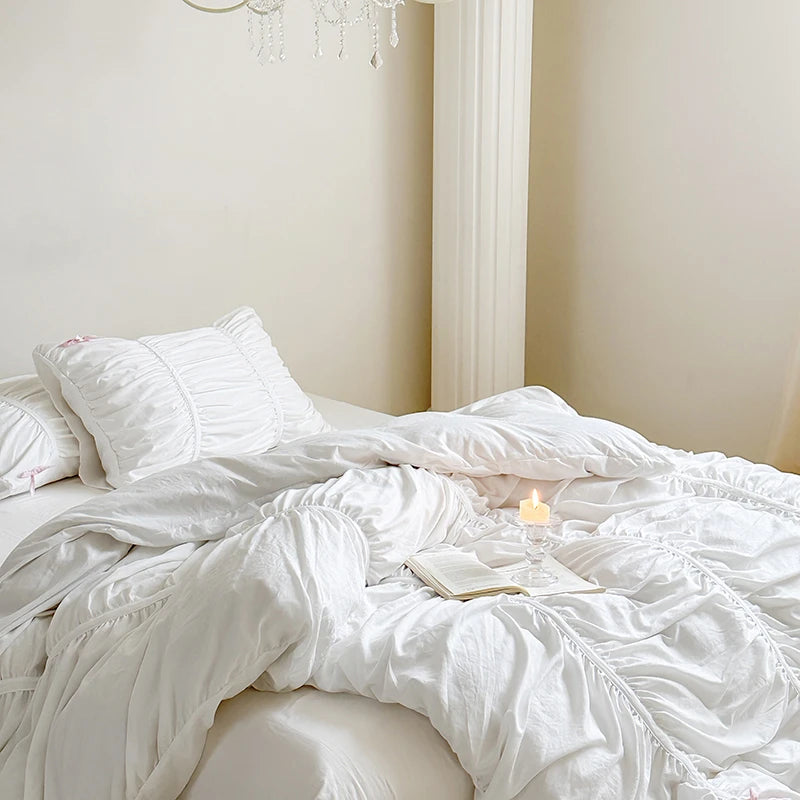 White bedding set on a bed with a candle and book in a softly lit room.
