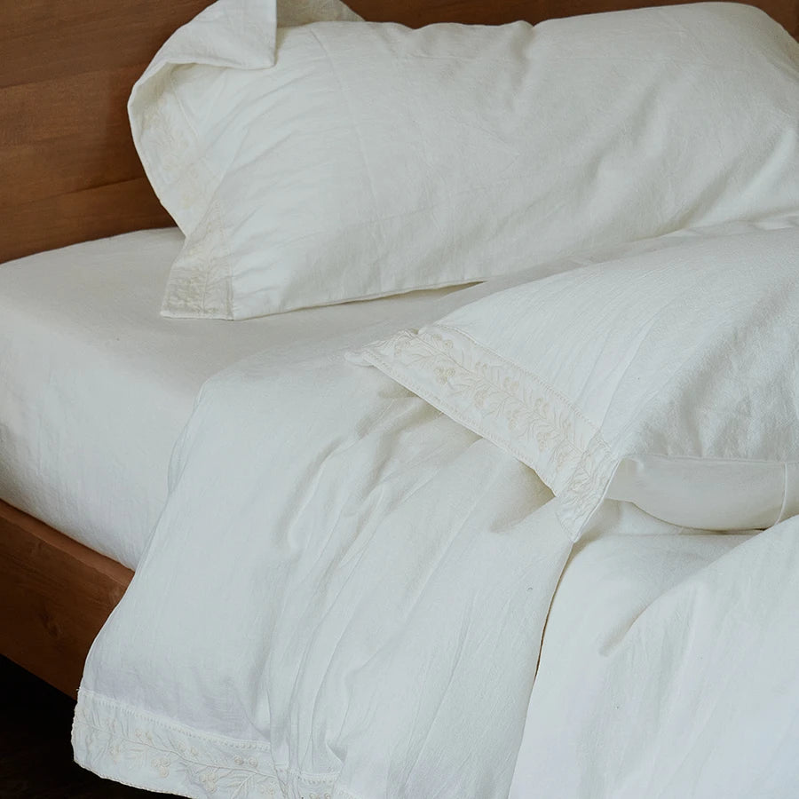 White bedding with floral embroidered lace pillows on a wooden bed frame.