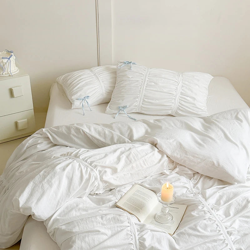 White bedroom with a bed featuring white bedding, pillows, and an open book with a candle.