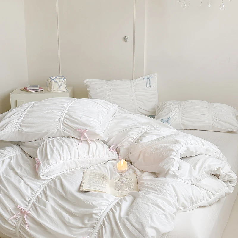 White comforter on a bed with a lit candle and book in a bedroom setting