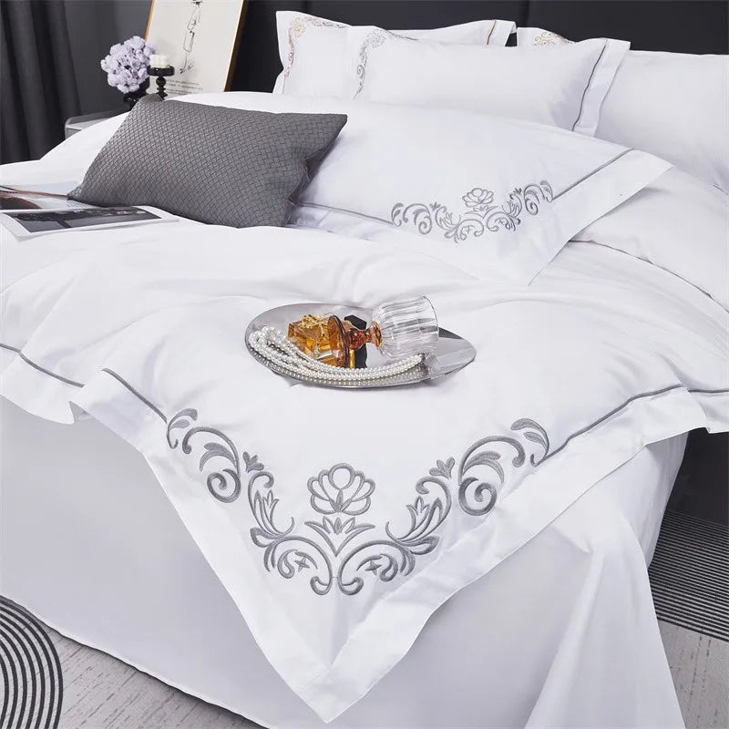 White embroidered bedding set on a bed with decorative pillows and a small table.