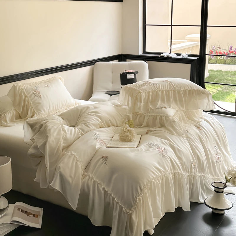 White ruffled bedspread on a bed in a well-lit room with a window.