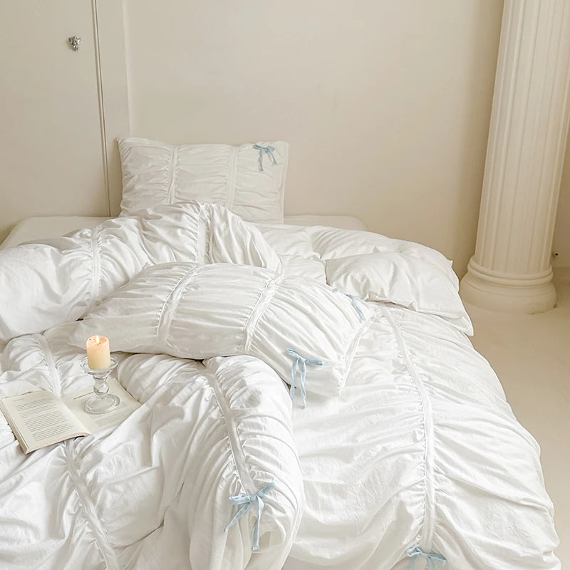 White textured comforter on a bed with a candle and book in a softly lit room.